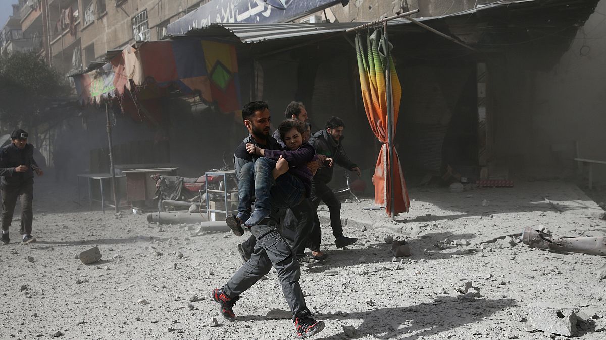 Ein Mann rennt mit einem Mädchen auf dem Arm nach einem Luftangriff.