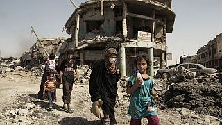 نساء وأطفال يتنقلون عبر حطام المباني والمركبات التي دمرت أثناء القتال