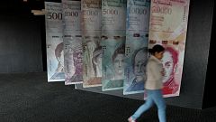 A woman walks by banners of Venezuelan bolivar
