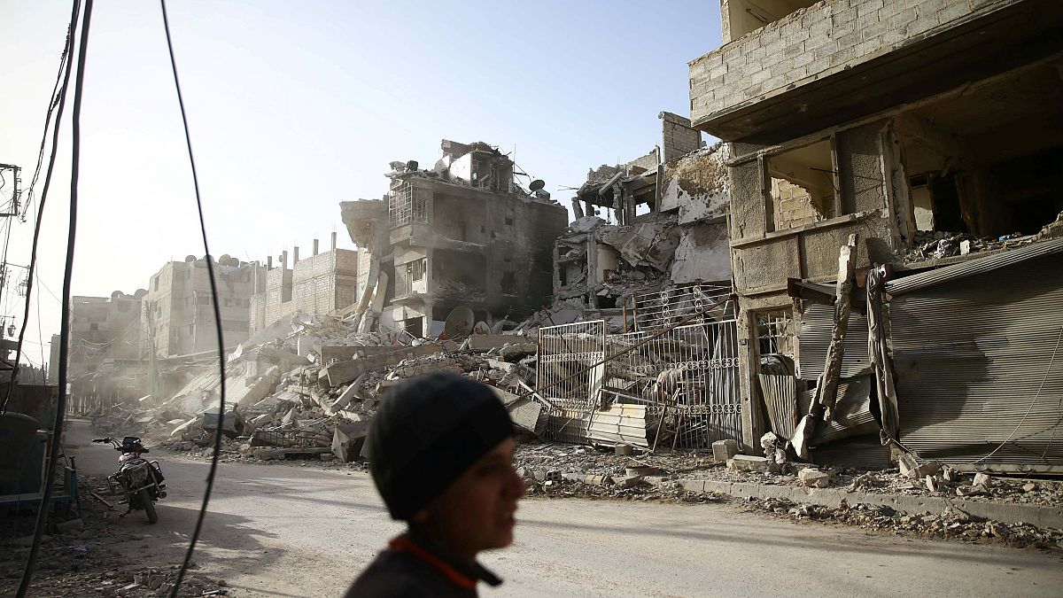 a boy walks near damaged buildings in the besieged town of Douma
