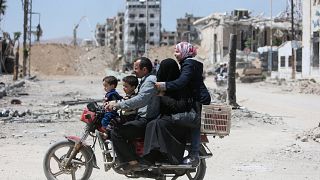 A Syrian family rides along a damaged street in Douma, Damascus.