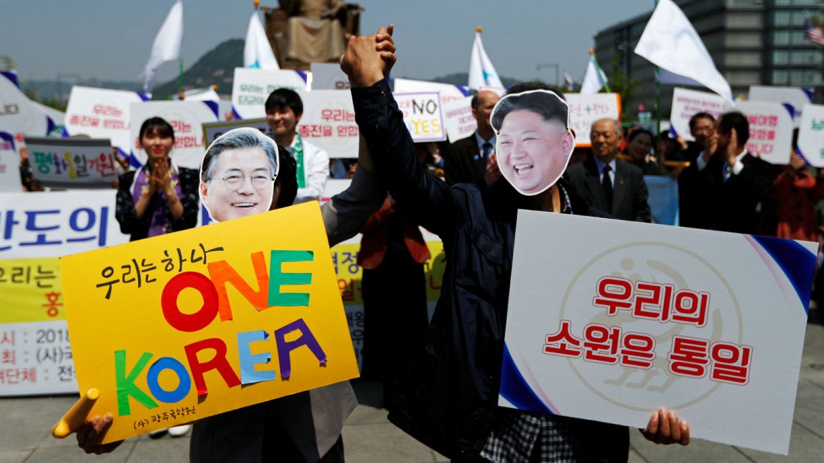 People hold hands as they wear masks of South Korea's President Moon Jae-in