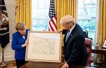 Merkel übergibt Trump eine Landkarte von Rheinland-Pfalz.