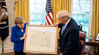 Merkel übergibt Trump eine Landkarte von Rheinland-Pfalz.