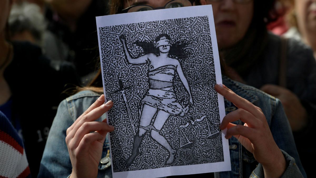A woman holds up a picture as other shout slogans during a protest 