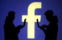 Silhouetten zweier Männer mit Laptop vor Facebook-Logo