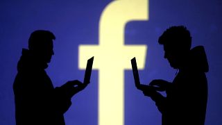 Silhouetten zweier Männer mit Laptop vor Facebook-Logo
