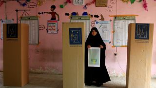 Eine Frau mit Stimmzettel neben den Wahlkabinen im Irak