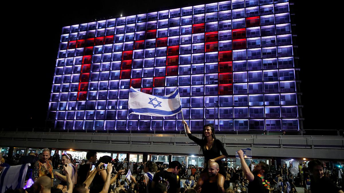 TOY-Lichtprojektion auf ein Hotel in Tel Aviv; Israel-Flaggenschwenkerin