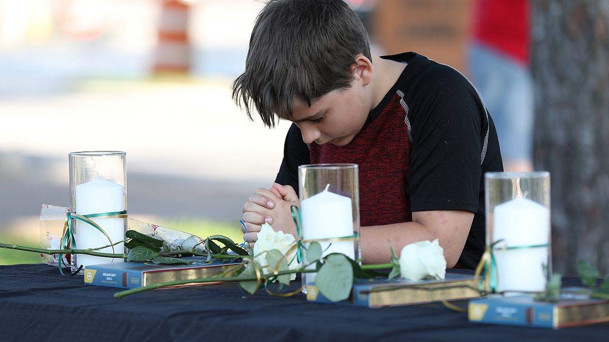 Ein Junge betet, drei weiße Kerzen stehen auf dem Tisch vor ihm.