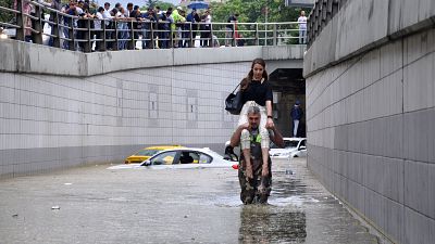 Man carries a woman on his shoulders at a flooded street