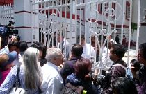 Mexikaner warten an weißem Gittertor auf Einlass