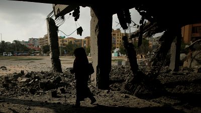 Woman passes a building that was destroyed by Israeli air strike