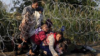 Syrian migrants cross under a fence as they enter Hungary