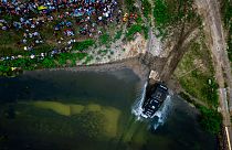 Vogelperspektive: Ein Truck fährt in ein Gewässer, viele Menschen schauen