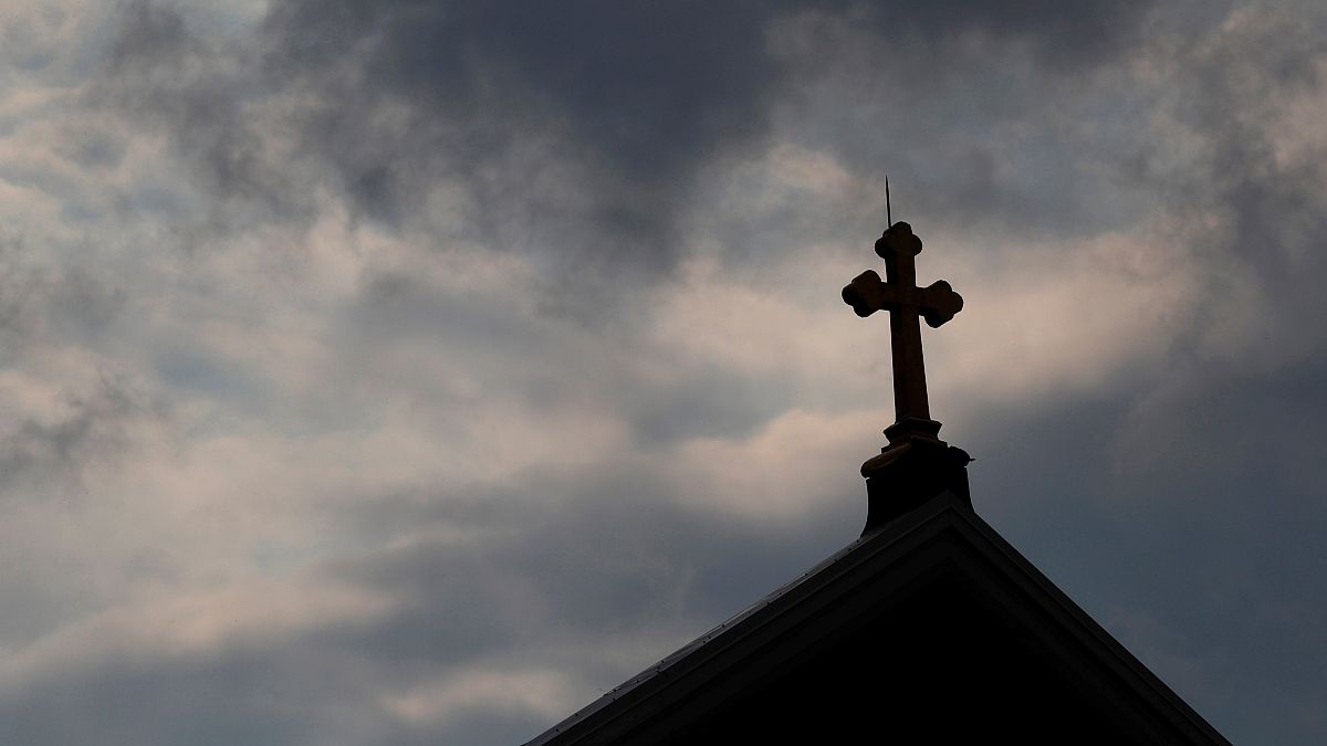 Kreuz auf Kirchendach vor dunklen Wolken