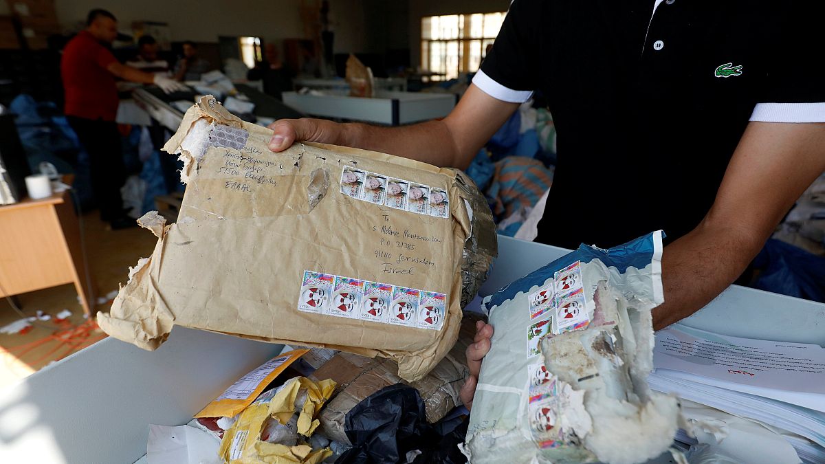 Ein Postmitarbeiter zeigt zwei beschädigte Päckchen