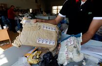 Ein Postmitarbeiter zeigt zwei beschädigte Päckchen