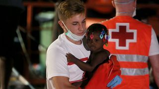 Un miembro de la Cruz Roja lleva a un niño migrante en brazos.