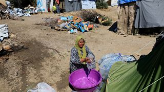 A migrant empties water into a bucket at a makeshift camp in Greece