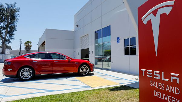 Ein roter Tesla und ein Schild mit dem Tesla-Logo Ein roter Tesla und ein Schild mit dem Tesla-Logo