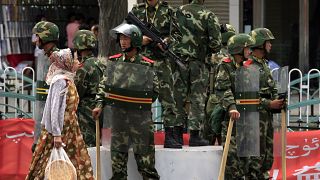 Doğu Türkistan'ın Urumçi kentinde, Çinli askerlerin önünden geçen Uygur kadın