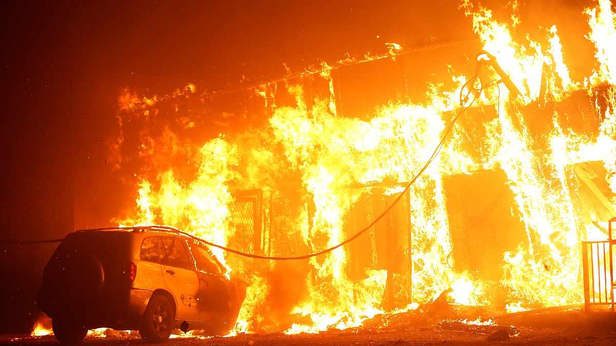 Ein Auto steht vor einem brennenden Haus