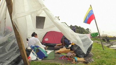 Venezolanische Migranten in einem Zelt, daneben die ven. Flagge