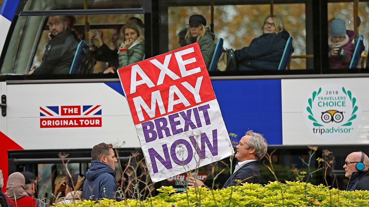 Ein Mann hält ein Plakat vor einem Touristenbus: "Axe May - Brexit now"