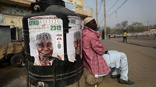 A man sits next to a campaign poster after Nigeria's elections are delayed.