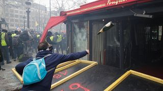 متظاهر يلقي بزجاجة على محل بباريس في احتجاجات السترات الصفراء الأسبوعية