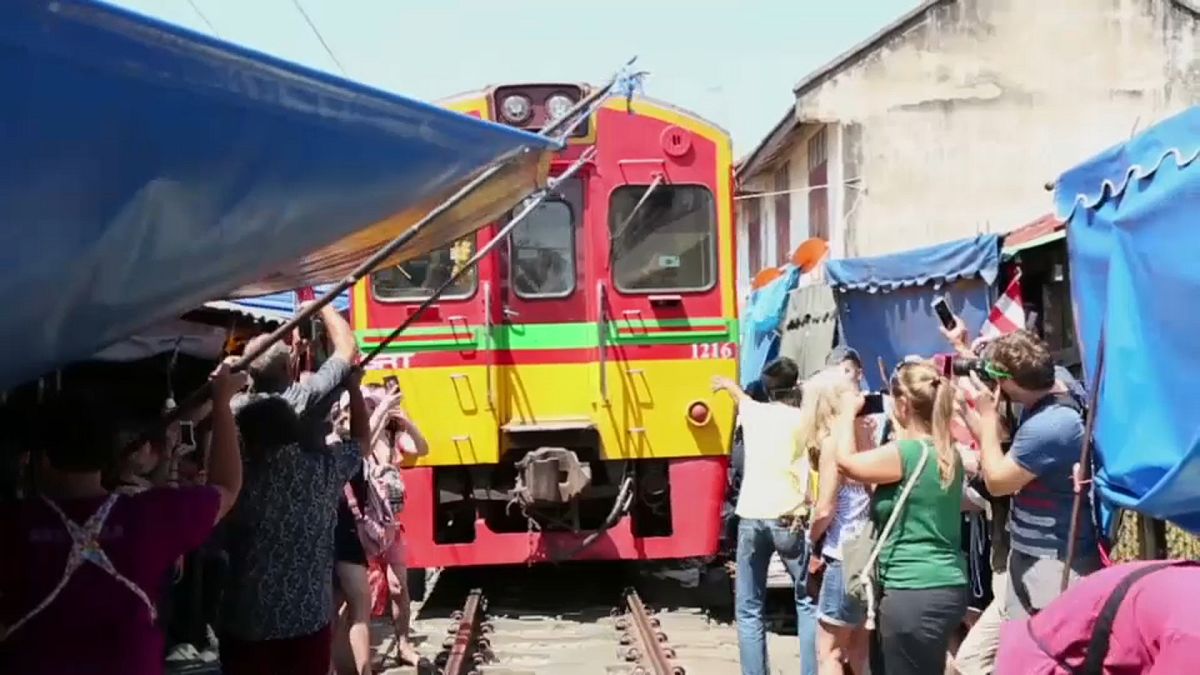 Market traders step aside as the train approaches while tourists step out