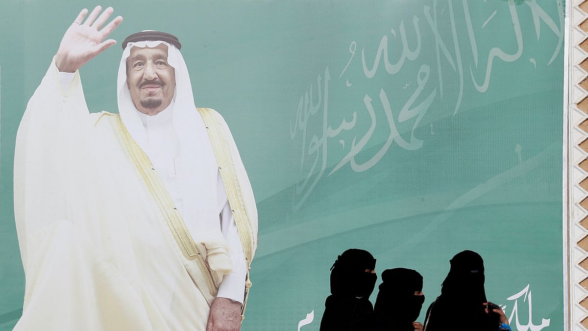 صورة عملاقة للملك سلمان وسيدات سعوديات ينظرن إلى الصورة 