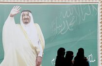 صورة عملاقة للملك سلمان وسيدات سعوديات ينظرن إلى الصورة 