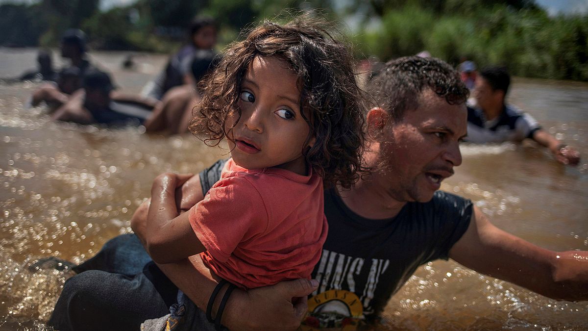 Ein Migrant aus Honduras hilft einem Kind über einen Fluss.