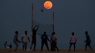 People play volleyball on the beach as the Pink Moon rises in the sky over