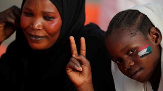 طفلة سودانية وعلى خدها رسمت علم السودان ترفع إشارة النصر رفقة أمها