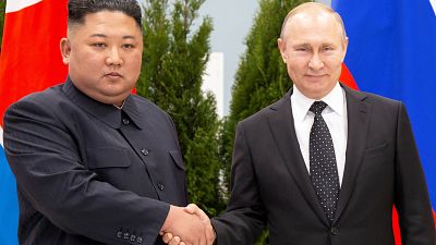 Kim Jong-un und Wladimir Putin schütteln sich vor ihren Landesflaggen Hände