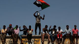 متظاهر سوداني يرتدي قناعا ويلوح بالعلم الوطني