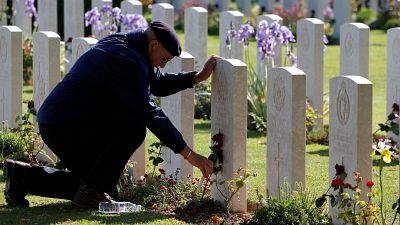 A man places a flower on a tomb at Commonwealth War Cemetery in Bayeux