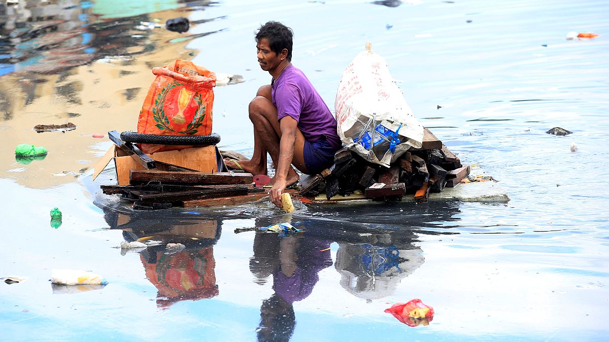 Man uses an improvised banca to collect plastic materials in a polluted river in Manila
