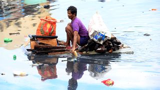 Man uses an improvised banca to collect plastic materials in a polluted river in Manila