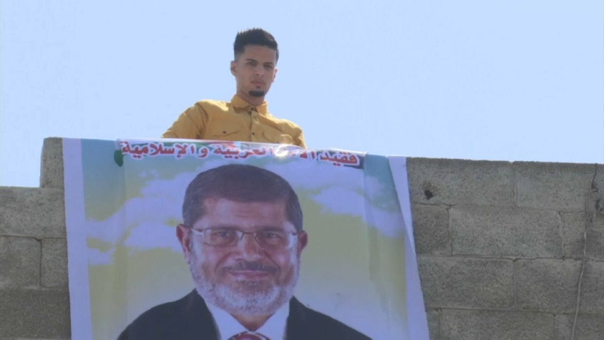 شاب يقوم بتعليق صورة كبيرة لرئيس مصر السابق محمد مرسي على حافة بناء في رفح بقطاع غزة