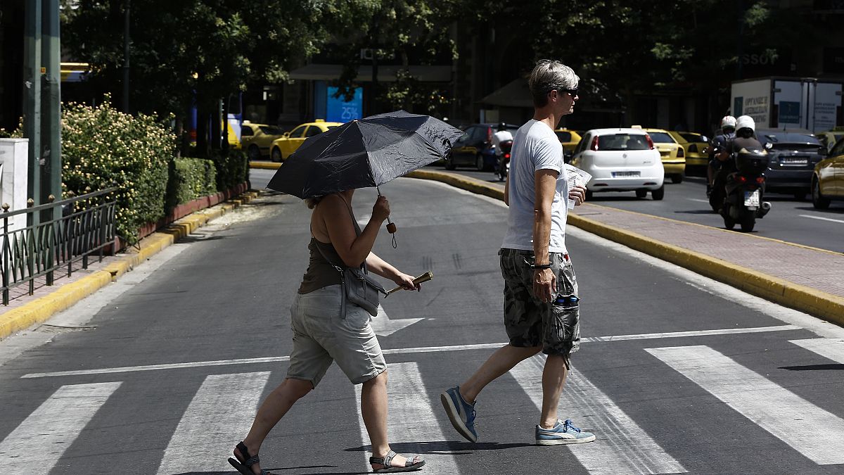 Ζευγάρι τουριστών περπατούν κρατώντας ομπρέλα για να προφυλαχτούν από τον ήλιο