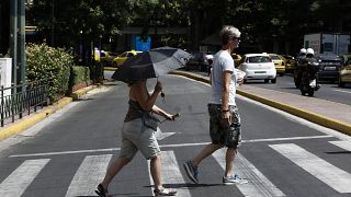 Ζευγάρι τουριστών περπατούν κρατώντας ομπρέλα για να προφυλαχτούν από τον ήλιο