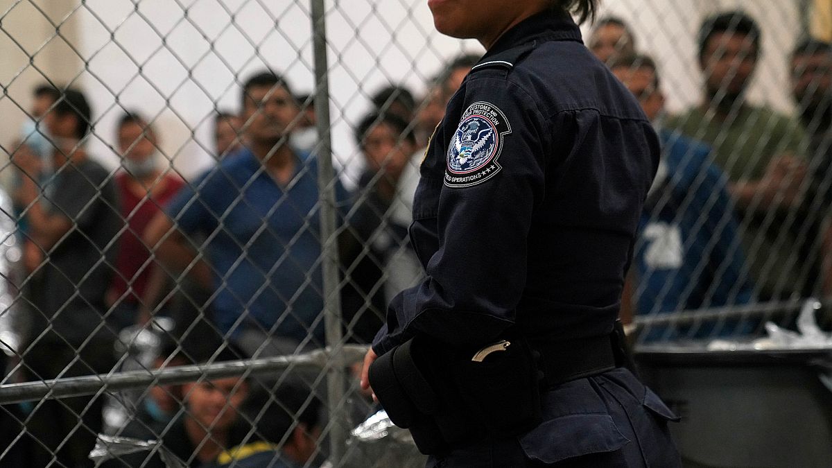 Single men wait behind caged wire at a detention facility in Texas on Friday