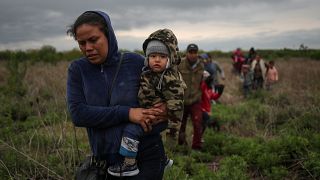 Ana María, de El Salvador, lleva en brazos a su hijo de un año, Mateo, mientras caminan por un campo con otros inmigrantes centroamericanos que buscan asilo.