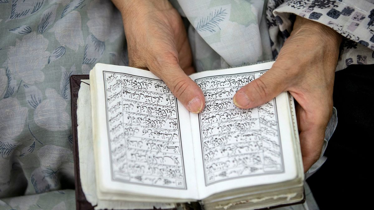 A woman prays while holding the Quran.