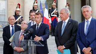 Frankreichs Präsident Macron neben Außenminister Le Drian und UN-Hochkommissar für Flüchtlinge Grandi