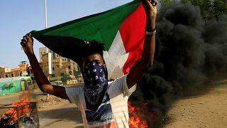 محتج ملثم يرفع علم السودان وخلفه إطارات تحترق أثناء احتجاج في العاصمة الخرطوم يوم 27 يوليو تموز 2019. تصوير: محمد نور الدين عبد الله